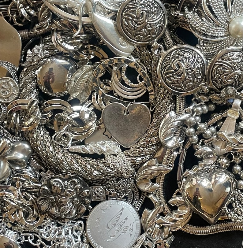 Puede incluir: Una colecci&oacute;n de joyas plateadas con diferentes formas y dise&ntilde;os, incluyendo corazones, flores y patrones geom&eacute;tricos. Las joyas est&aacute;n hechas de metal y tienen un acabado brillante.