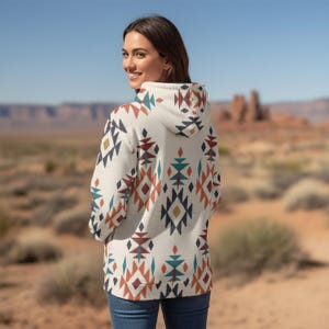 May include: A long-sleeved hooded sweatshirt in an off-white base color featuring a repeating geometric pattern in shades of dark blue, terracotta orange, teal, and mustard yellow. The hoodie includes a drawstring hood and a kangaroo pocket.