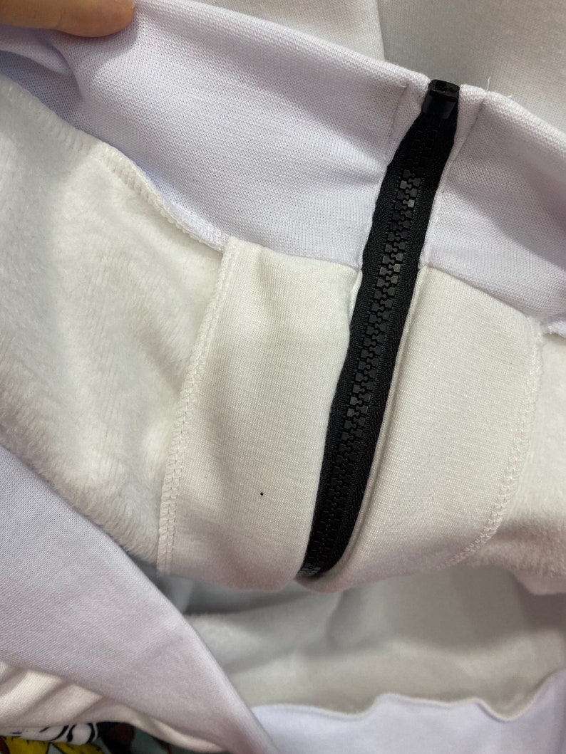 May include: Close-up of a white zipper on a white garment. The zipper is black and has a metal slider.