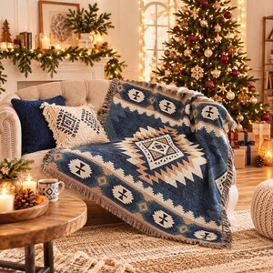 Op de afbeelding: Een geweven plaid met een geometrisch patroon in blauw, cr&egrave;me en bruin met franjes, gedrapeerd over een bank naast een effen marineblauw kussen en een cr&egrave;mekleurig, getextureerd kussen met een donkerblauw ruitpatroon.