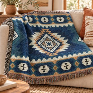 Op de afbeelding: Een geweven plaid met een diepblauwe achtergrond en een groot centraal ruitpatroon in tinten beige, cr&egrave;me en donkerblauw. De deken heeft een decoratieve rand met geometrische vormen en een franje aan de onderkant.