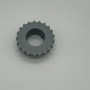 Puede incluir: Un engranaje circular gris con dientes espaciados uniformemente alrededor del borde exterior. El engranaje tiene un agujero central y está hecho de un material sólido y mate. El objeto está aislado sobre un fondo blanco liso.