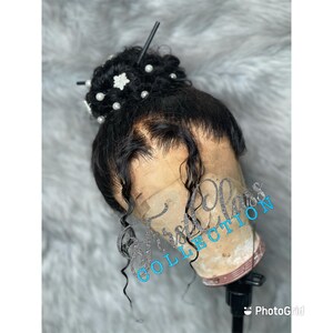 May include: A black human hair wig with a lace front, styled in a high bun with pearl and flower embellishments. The wig is on a mannequin head.