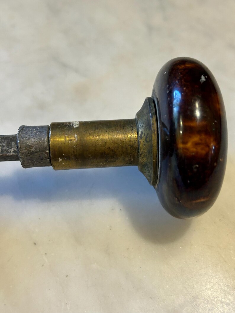 May include: Close-up of a vintage door knob. The knob has a dark brown, oval-shaped handle with a mottled pattern. The handle is attached to a brass and metal mechanism.