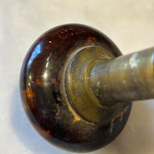 May include: Close-up of a vintage door handle. The handle features a dark brown, glossy, rounded knob with a mottled pattern. The base is brass-colored, and the metal arm extends to the right. The handle shows signs of age and wear.
