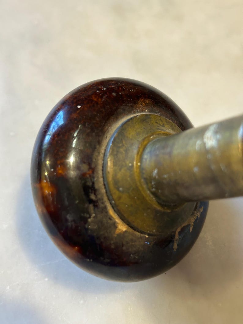 May include: Close-up of a vintage door handle. The handle features a dark brown, glossy, rounded knob with a mottled pattern. The base is brass-colored, and the metal arm extends to the right. The handle shows signs of age and wear.