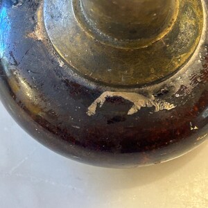 May include: Close-up of a vintage door knob. The knob features a dark brown, rounded base with visible wear and a brass-colored metal stem and circular plate. The finish shows signs of age and use, adding to its antique charm.
