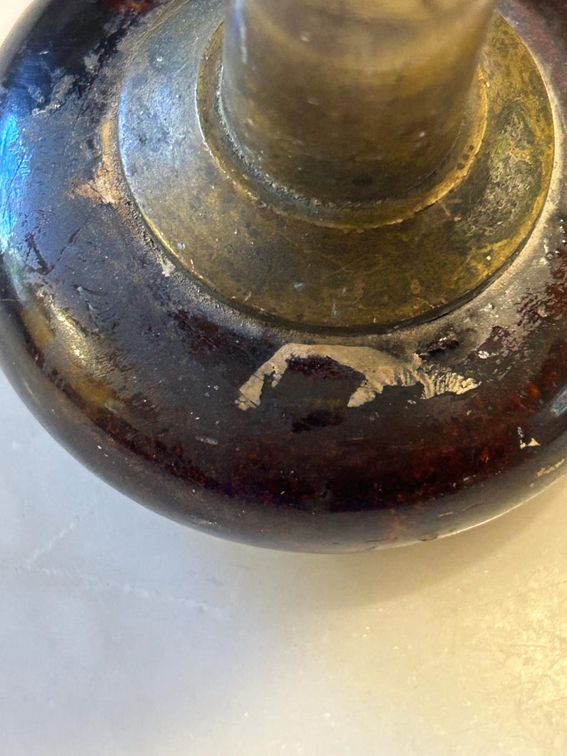 May include: Close-up of a vintage door knob. The knob features a dark brown, rounded base with visible wear and a brass-colored metal stem and circular plate. The finish shows signs of age and use, adding to its antique charm.