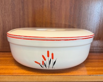 Puede incluir: Plato para hornear de cerámica blanca con un borde rojo y un diseño de espadañas negro y naranja. El plato tiene una tapa.