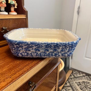 May include: A rectangular ceramic baking dish with a cream-colored interior and a blue and white sponge-painted exterior pattern. The dish features slightly rounded corners and a smooth, glossy finish, designed for oven use and food preparation.