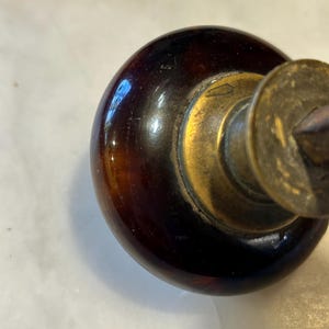 May include: Close-up of a vintage door knob. The knob is a dark, glossy brown with a brass base and a circular brass plate. The knob has a rounded shape and a smooth, reflective surface.