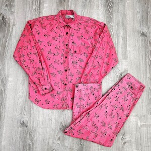 May include: A pink button-up shirt and matching pants with a black bird print. The shirt has a collar and long sleeves. The pants have a straight leg.