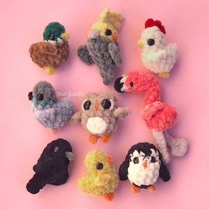 Puede incluir: Una colección de nueve peluches de animales de crochet en varios colores, incluyendo un pato, un loro, una gallina, un flamenco, un búho, un pingüino y un pollito. Los peluches están hechos de hilo y tienen un aspecto suave y texturizado.