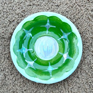 May include: A green ceramic dish with a light blue rim and a white center. The dish has a scalloped edge and is decorated with eight blue star-shaped designs.