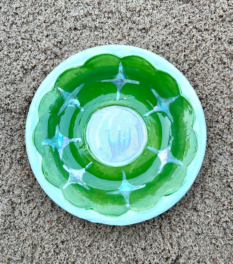 May include: A green ceramic dish with a light blue rim and a white center. The dish has a scalloped edge and is decorated with eight blue star-shaped designs.