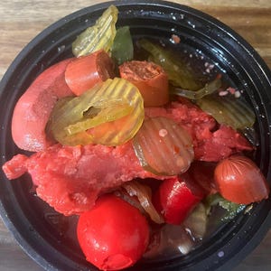 May include: A black plastic container filled with a variety of pickled foods, including red sausage, red peppers, green pickles, and yellow pickles.