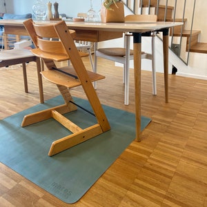 Può includere: Una moderna sala da pranzo con un tavolo e sedie in legno. Un seggiolone è appoggiato su un tappetino verde. Bottiglie di vino, bicchieri e oggetti decorativi sono sul tavolo. Una scala e una ghirlanda sono sullo sfondo.