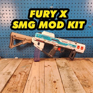 May include: A white and blue Nerf Fury X SMG mod kit with a tan stock and a clear magazine. The kit has a black grip and a red safety switch. The text "Fury X SMG Mod Kit" is written in yellow letters on a black background.