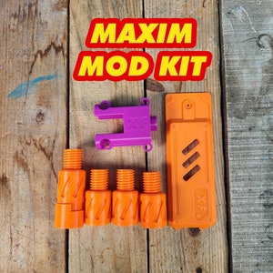 May include: A collection of orange and purple plastic components, including cylindrical pieces, a rectangular piece, and a bracket, arranged on a wooden surface. The text "MAXIM MOD KIT" is displayed in a red and yellow banner.