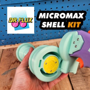 May include: A teal blue 3D printed shell kit for a Micromax toy gun. The kit includes a handle, a barrel, and a magazine. The kit is being held in a person's hand.