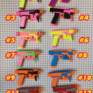 May include: Twelve toy guns in various colors and designs, numbered 1 through 12, displayed on a white pegboard.