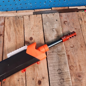 May include: A black and orange toy gun with a white barrel extension and a red and black barrel attachment. The gun is lying on a wooden surface.