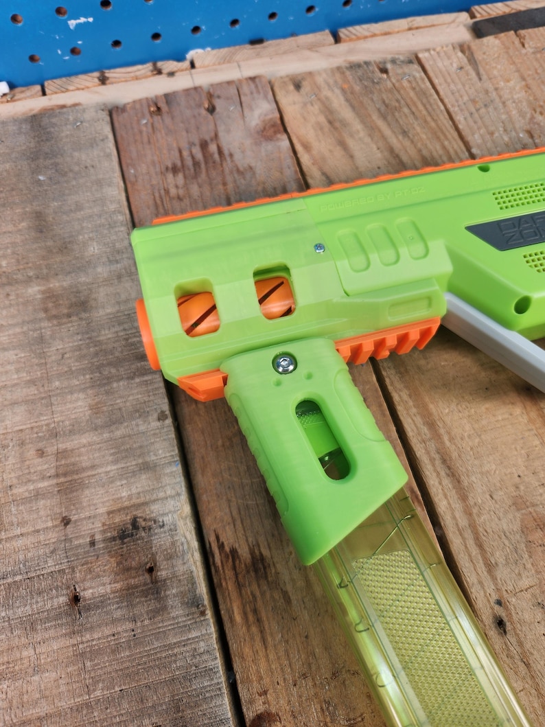K&ouml;nnte beinhalten: Eine gr&uuml;ne und orangefarbene Spielzeugpistole mit einem transparenten Magazin. Die Spielzeugpistole hat ein rechteckiges Design mit Griff und Abzug. Die Pistole ist aus Kunststoff und hat ein paar sichtbare Schrauben.