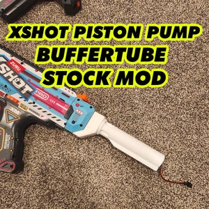 May include: A modified XShot toy gun with the text "XSHOT PISTON PUMP BUFFER TUBE STOCK MOD". The gun features a blue, white, and black color scheme with orange accents. The image is taken on a carpeted surface.