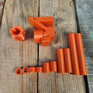 Puede incluir: Un conjunto de piezas de pl&aacute;stico naranja impresas en 3D, que incluye una pieza grande con forma curva, una pieza m&aacute;s peque&ntilde;a con forma redonda y varias piezas cil&iacute;ndricas m&aacute;s peque&ntilde;as.
