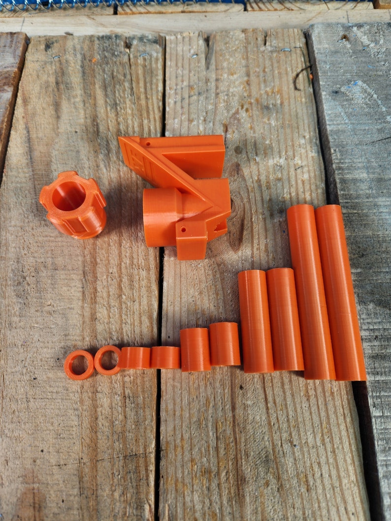 Puede incluir: Un conjunto de piezas de pl&aacute;stico naranja impresas en 3D, que incluye una pieza grande con forma curva, una pieza m&aacute;s peque&ntilde;a con forma redonda y varias piezas cil&iacute;ndricas m&aacute;s peque&ntilde;as.