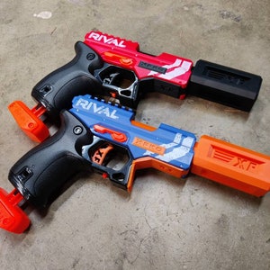 May include: Two Nerf Rival blasters, one red and one blue, with black grips and orange barrels. Both blasters have the word "RIVAL" printed on the side and the text "XFKO" printed on the top.