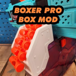 May include: A close-up of a Boxer Pro Box Mod. The mod is primarily teal and white, with orange cylindrical components. The text "BOXER PRO BOX MOD" is displayed in orange letters with a black outline.