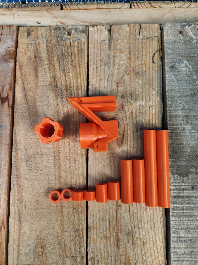 Puede incluir: Un conjunto de piezas de pl&aacute;stico naranja para un modelo impreso en 3D. El conjunto incluye una pieza grande con forma curva, una pieza m&aacute;s peque&ntilde;a con forma circular y varias piezas cil&iacute;ndricas de diferentes longitudes.