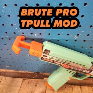 May include: A mint green and orange toy gun with the text "BRUTE PRO TPULL MOD" in a black and orange font. The toy gun is set against a blue pegboard background and wooden surface.