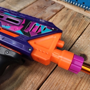 May include: A purple and orange toy gun with a camouflage pattern. The gun has a black grip and a pink barrel tip.