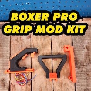 May include: A kit with the text "BOXER PRO GRIP MOD KIT" includes black and orange components. The kit features a handle, trigger, and other parts, along with a bundle of colorful wires. The items are displayed on a wooden surface.