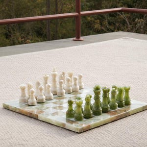 Op de afbeelding: Een schaakspel met een groen en wit marmeren bord. De schaakstukken zijn wit en groen. Het bord is opgesteld, klaar voor een spel. De achtergrond is neutraal.