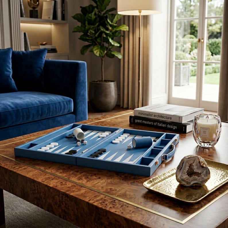 May include: A blue backgammon set with white and black game pieces sits on a wooden coffee table. The set is open, displaying the playing surface. A gold tray with a geode and a candle are also on the table.