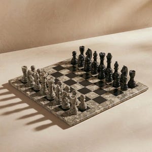 May include: A marble chess set with black and gray pieces arranged on a checkered board. The board is made of marble with black and gray squares. The chess pieces are black and gray.