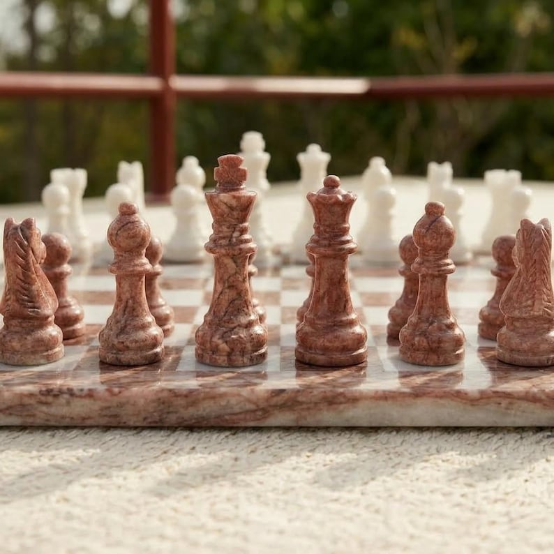 Puede incluir: Un juego de ajedrez de m&aacute;rmol con piezas pulidas en tonos marr&oacute;n rojizo y blanco. El tablero est&aacute; construido con cuadrados de m&aacute;rmol a juego. El conjunto incluye piezas talladas de rey, reina, alfil, caballo y pe&oacute;n sobre el tablero.