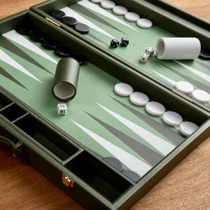 May include: An open, olive green backgammon set with white and black game pieces. The board has a green and white pattern. Dice and dice cups are visible, suggesting a game in progress.