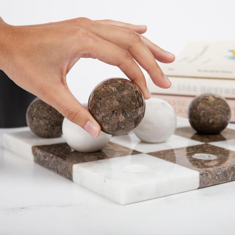 May include: A marble checkerboard game set with brown and white marble playing pieces. The board has a checkered pattern with alternating brown and white squares.