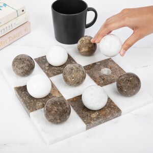 May include: A marble checkerboard game set with brown and white marble pieces. The board is made of white marble with brown marble squares. The pieces are round and have a mottled brown or white color.
