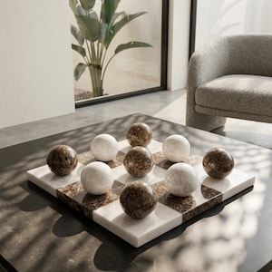May include: A square game board featuring a checkered pattern of alternating white and dark brown marble squares. Nine polished marble spheres are arranged on the board, with five dark brown spheres and four white spheres placed in a grid.