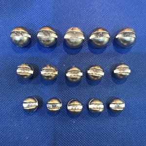May include: A collection of 15 silver-colored fishing sinkers, arranged in three rows. The sinkers are round and have a small hole in the top for attaching a fishing line.