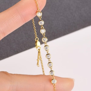 May include: A delicate gold necklace featuring seven round, clear gemstones. The necklace has a fine chain and a small clasp. The gemstones are evenly spaced along the chain, creating a simple yet elegant design.