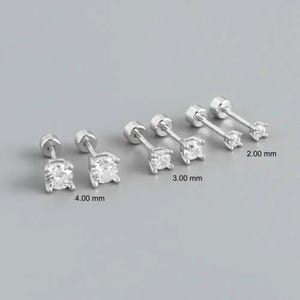 Könnte beinhalten: Silberne Ohrstecker mit klaren Zirkonia-Steinen. Die Ohrringe werden in drei Größen gezeigt: 2,00 mm, 3,00 mm und 4,00 mm. Die Ohrringe haben einen Schraubverschluss und sind auf grauem Hintergrund.