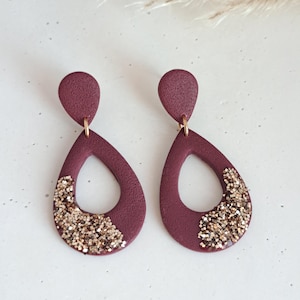 Può includere: Un paio di orecchini a forma di goccia di colore marrone rossiccio con dettagli di glitter dorati.
