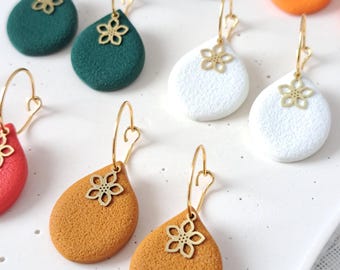 May include: A collection of teardrop-shaped earrings in various colors including black, orange, dark green, white, red, and mustard yellow. Each earring features a textured surface and a gold-toned metal hoop with a small, flat flower charm.