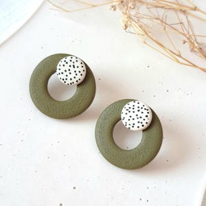 Può includere: Un paio di orecchini a cerchio verde oliva con un cerchio bianco con pois neri al centro di ogni orecchino.